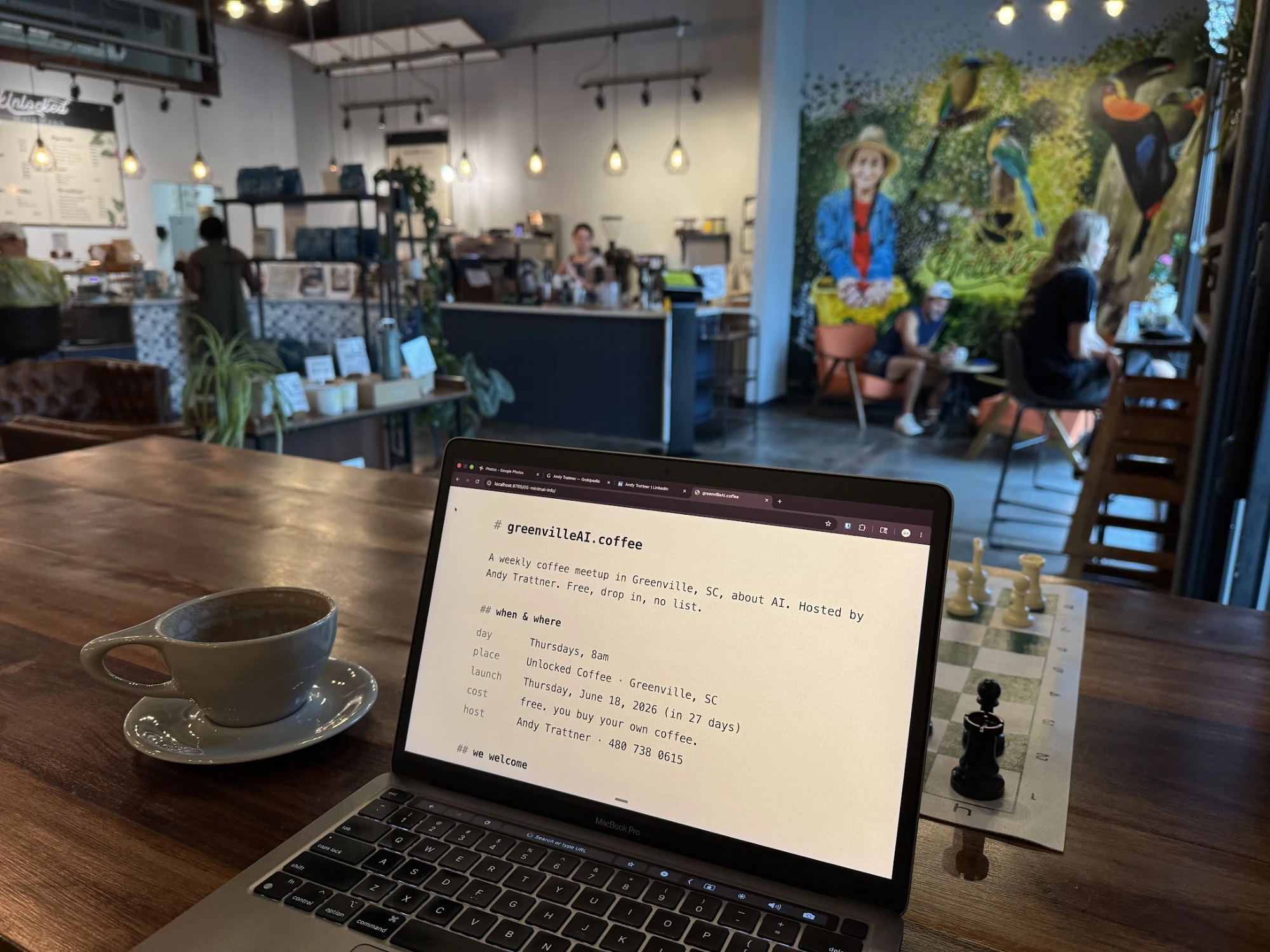 Wide view of Unlocked Coffee interior with the parrot/toucan mural, a latte cup, a chess board, and a laptop on the wooden table.